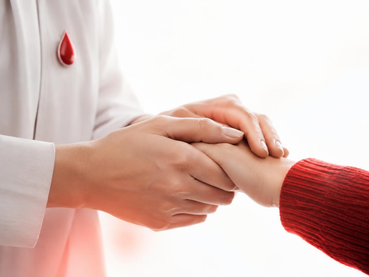 A healthcare volunteer holding a patient's hand, with a red blood-drop pin